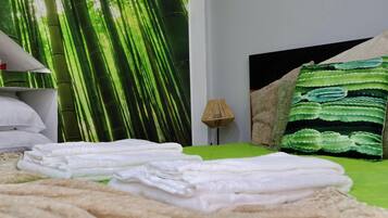 Una cama bien hecha con sábanas blancas, una colcha verde y una almohada verde y blanca a rayas.