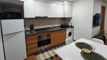 A compact kitchen with white cabinets, a built-in microwave, a washing machine, and a dining area with a table and chairs.