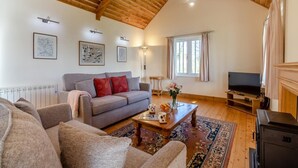 Uma sala de estar com sofá, mesa de centro, TV, lareira e vigas de madeira no teto.