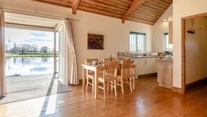 Um quarto espaçoso com piso de madeira, uma mesa de jantar com cadeiras, uma cozinha e uma grande janela com vista para a água.