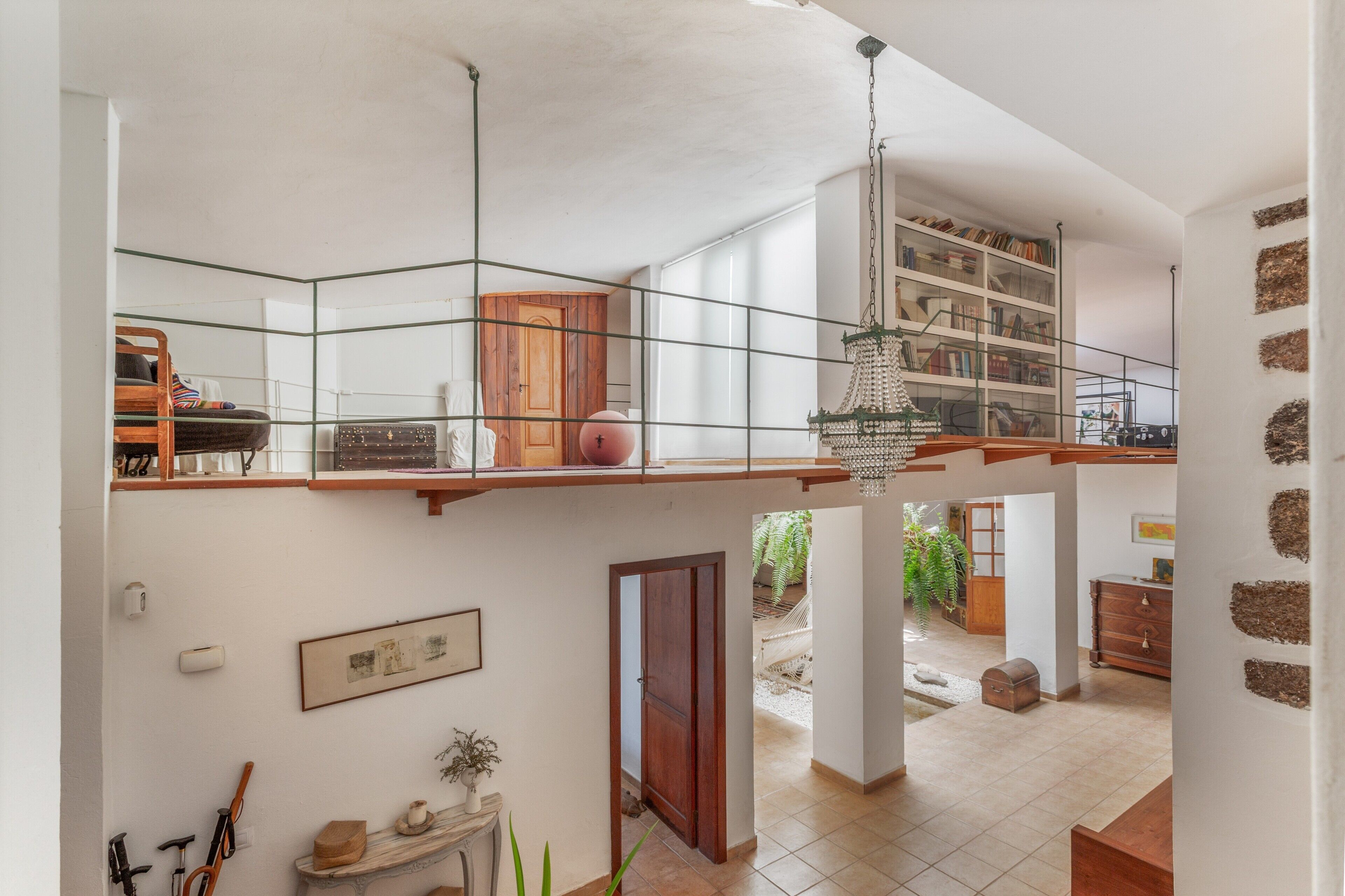 Un intérieur spacieux avec un plafond haut, un lustre suspendu et une vue sur un jardin par une porte ouverte.