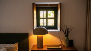 A bedside table with a lamp, a small window, and a vase with sticks. - Casa Rosa Chalet with Shared Pool, Wi-Fi and Air Conditioning (São João da Pesqueira)