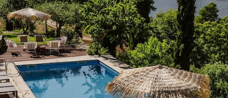 Una piscina con sillas de descanso y una mesa, rodeada de vegetación y vistas a colinas.
