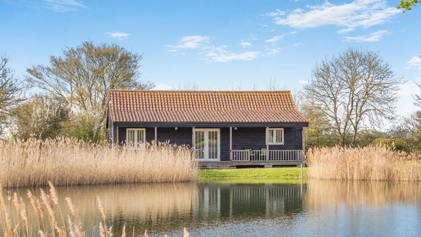 Une maison avec un toit en tuiles, un porche et son reflet dans l’eau.