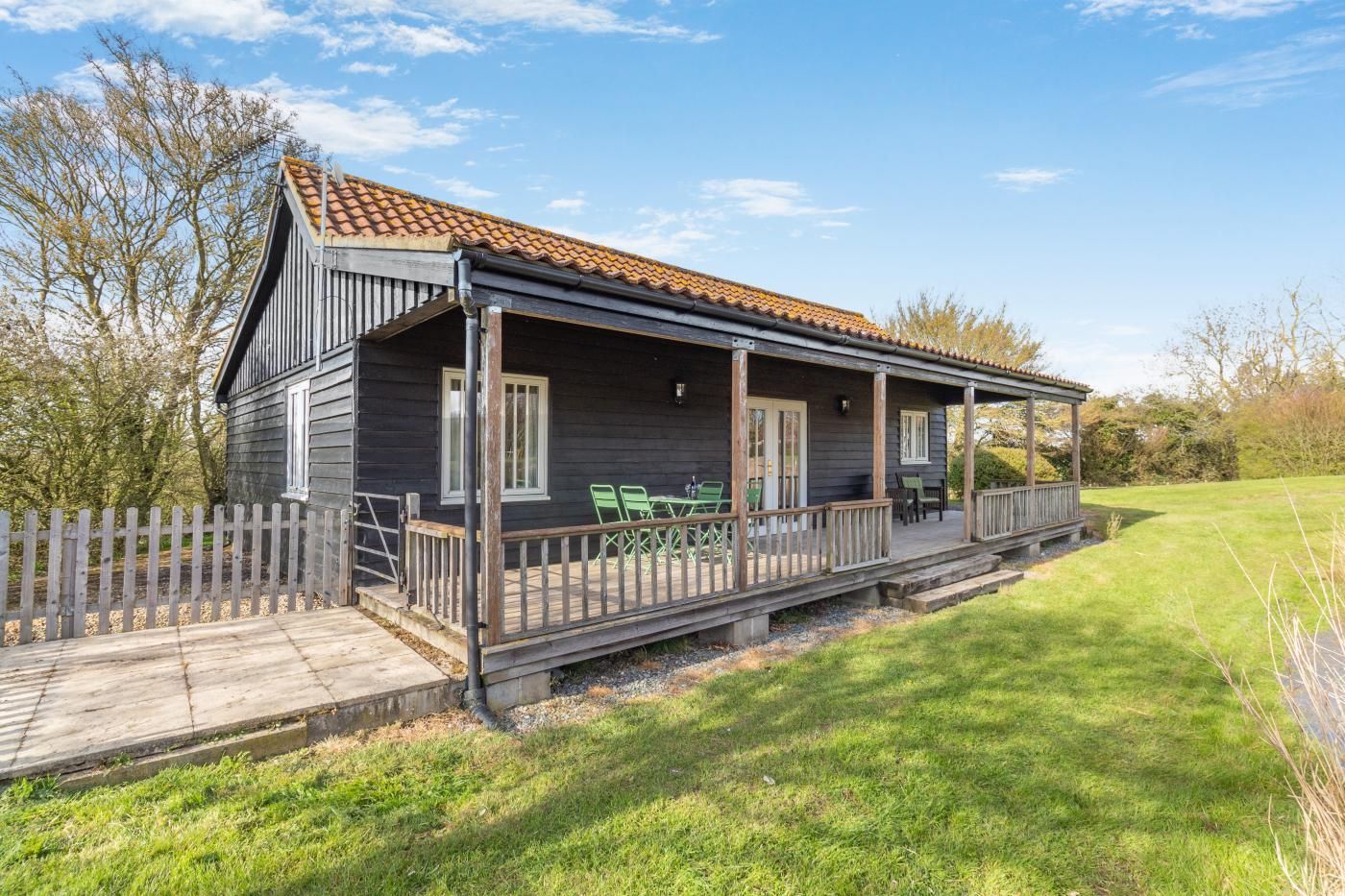 A wooden cabin with a porch, a fenced yard, and a clear sky.