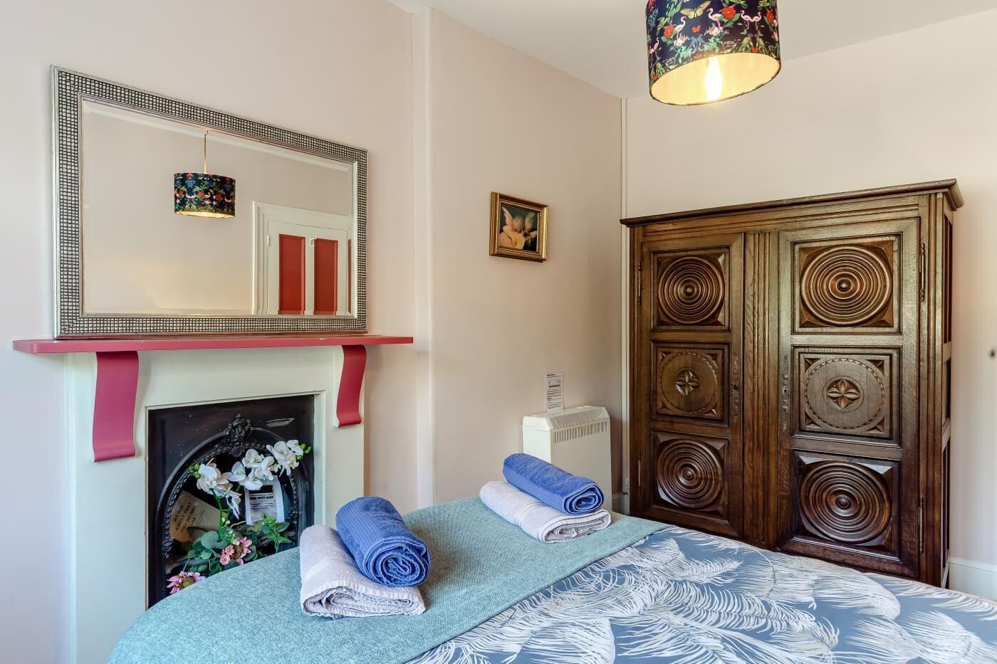 Une chambre avec une cheminée, un grand miroir, une armoire en bois et un lit avec des serviettes enroulées.
