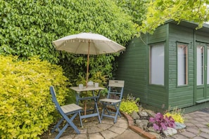 A patio with a table and chairs, a white umbrella, and a green building. - 3 Bed in Henstridge (oc-s40246) (Henstridge)