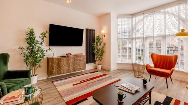 Un salon moderne doté d’un téléviseur à écran plat, d’un canapé, d’un fauteuil, d’une table basse et d’une grande fenêtre avec des stores.