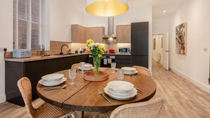 Une cuisine moderne avec des meubles en bois, une table à manger dressée avec des assiettes, des verres et un vase de fleurs.