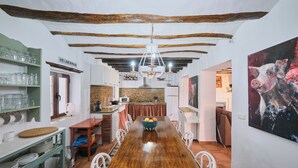 A dining area with a long wooden table, white chairs, a chandelier, and a painting on the wall.
