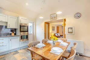 A modern kitchen with built-in appliances and a dining area with a wooden table set for four. - 3 Bed in Poolewe (oc-r38637) (Poolewe)