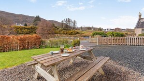Une table de pique-nique installée à l’extérieur, offrant une vue sur un paysage rural, avec des collines et une maison au loin.