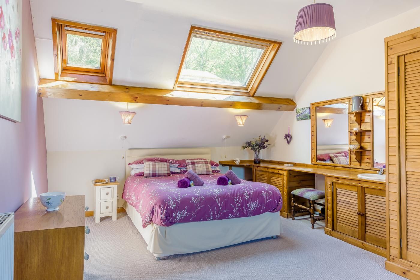 Ein Schlafzimmer mit Bett, Schreibtisch, Spiegel und einem Dachfenster.
