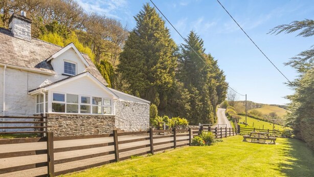 A white stone building with a wooden fence, a grassy area, and a picnic table. - 4 Bed in Builth Wells (oc-t38238) (Treflys)