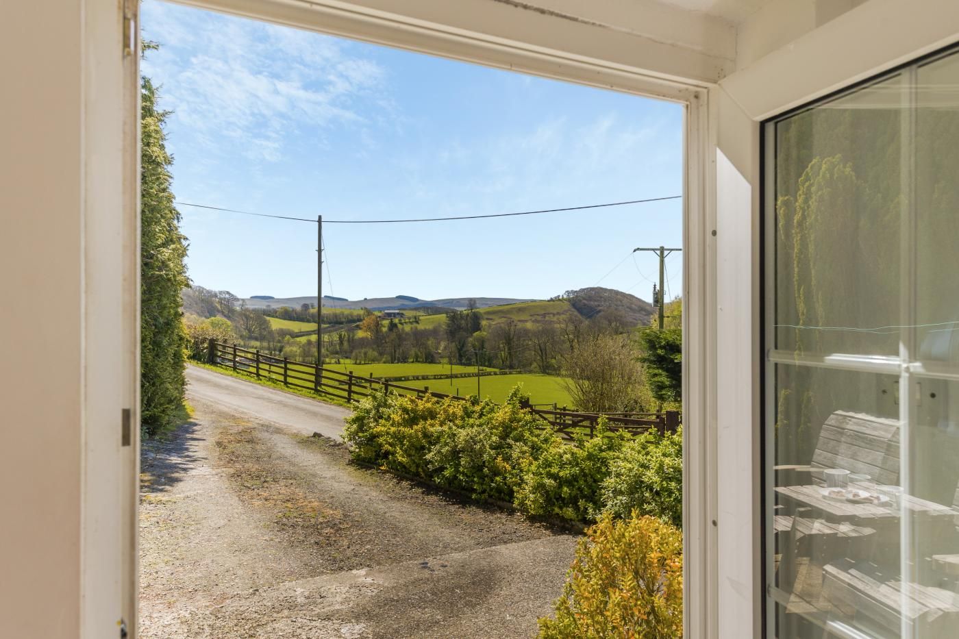 A view from a room with a door leading to a rural road, surrounded by greenery and hills.