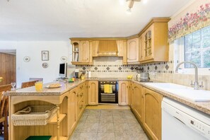 A kitchen with wooden cabinets, a built-in oven, a Bosch dishwasher, and a window with a floral view. - 4 Bed in Builth Wells (oc-t38238) (Treflys)