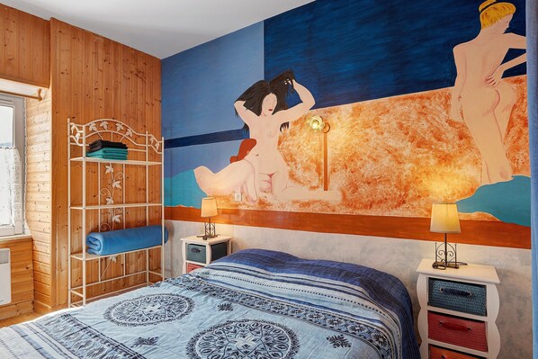 A room with a bed, a wooden wardrobe, a nightstand, and a wall painting.