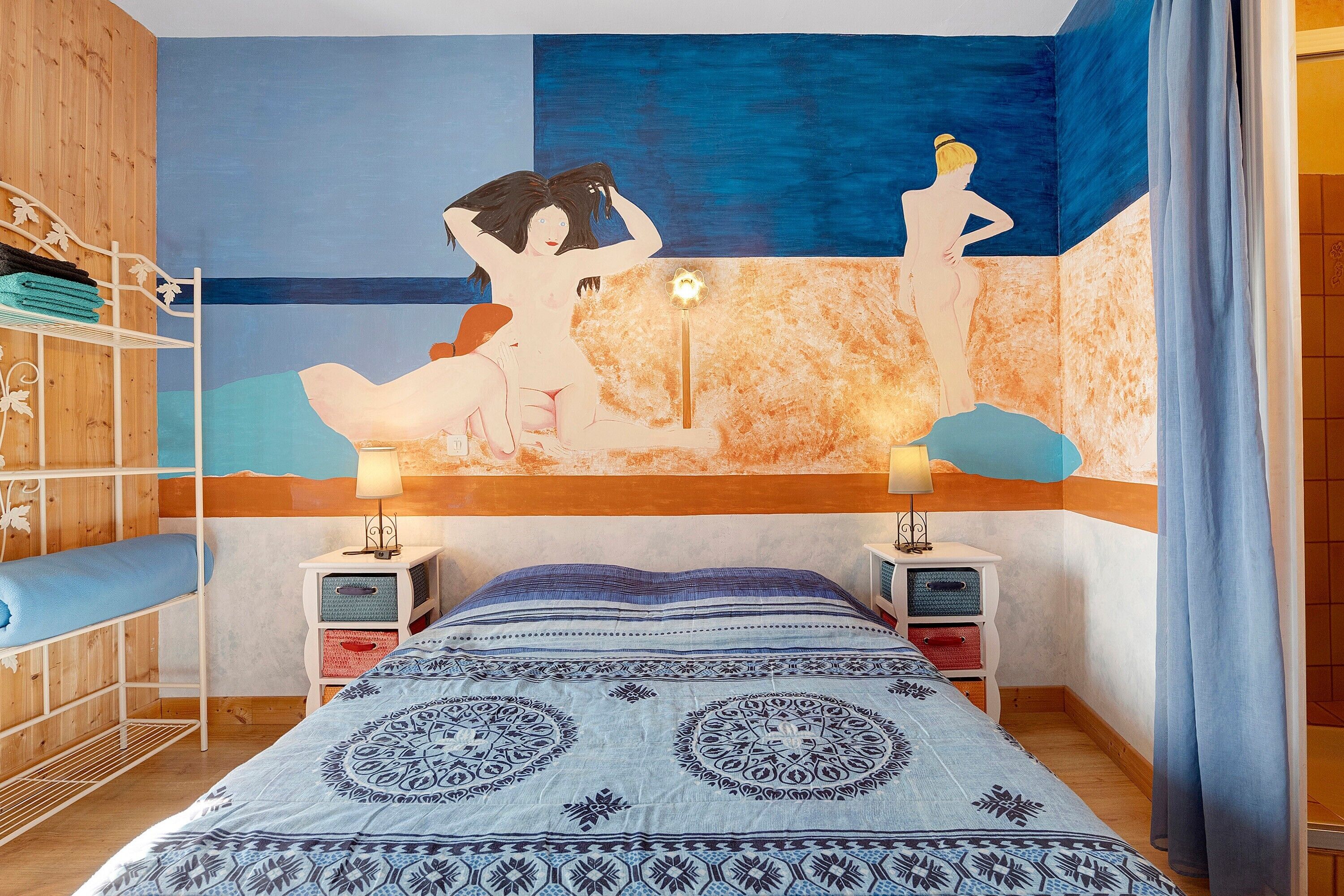 Une chambre à coucher avec un lit, deux tables de chevet, un mur orné d’un tableau, une armoire en bois et un rideau.