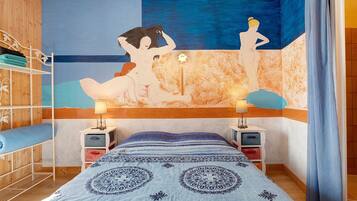 Une chambre à coucher avec un lit, deux tables de chevet, un mur orné d’un tableau, une armoire en bois et un rideau.