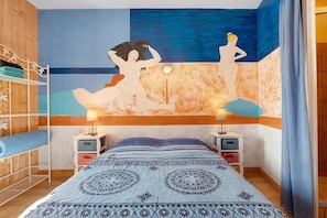 Une chambre à coucher avec un lit, deux tables de chevet, un mur orné d’un tableau, une armoire en bois et un rideau.