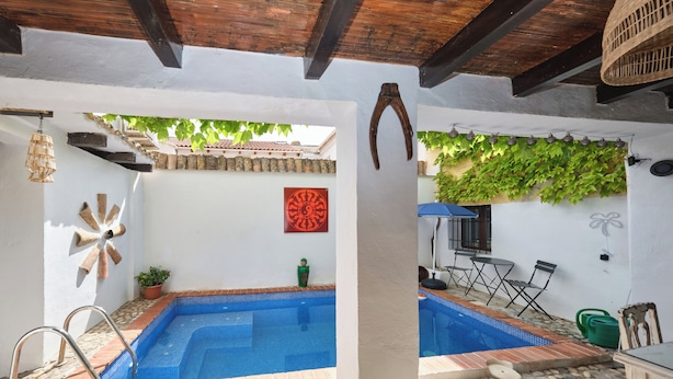 A swimming pool with a tiled edge, a wooden deck, a table with chairs, and a wall with a decorative pattern. - Luxury bedroom in Los Bermejales with a view of the pool. (Fornes)