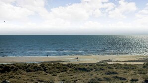 A beach with a clear sky, calm sea, and a few people in the distance. - 8 Bed in Barmouth (oc-89784) (Barmouth)
