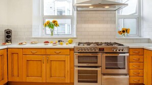 A kitchen with wooden cabinets, a gas stove, two ovens, and windows with sunflowers. - 8 Bed in Barmouth (oc-89784) (Barmouth)