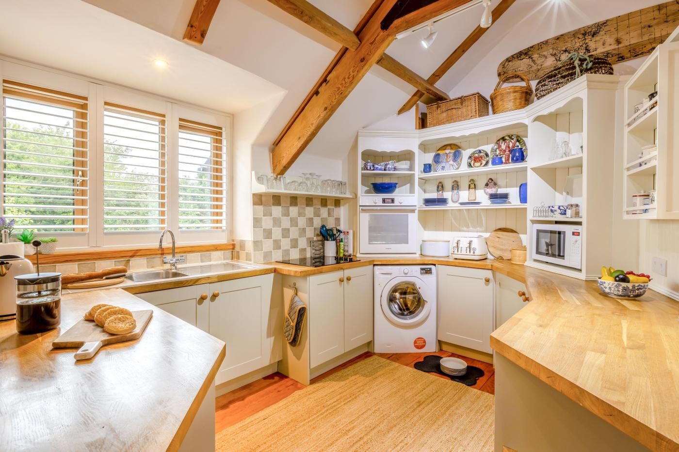 A kitchen with wooden beams, a washing machine, and a window with blinds.