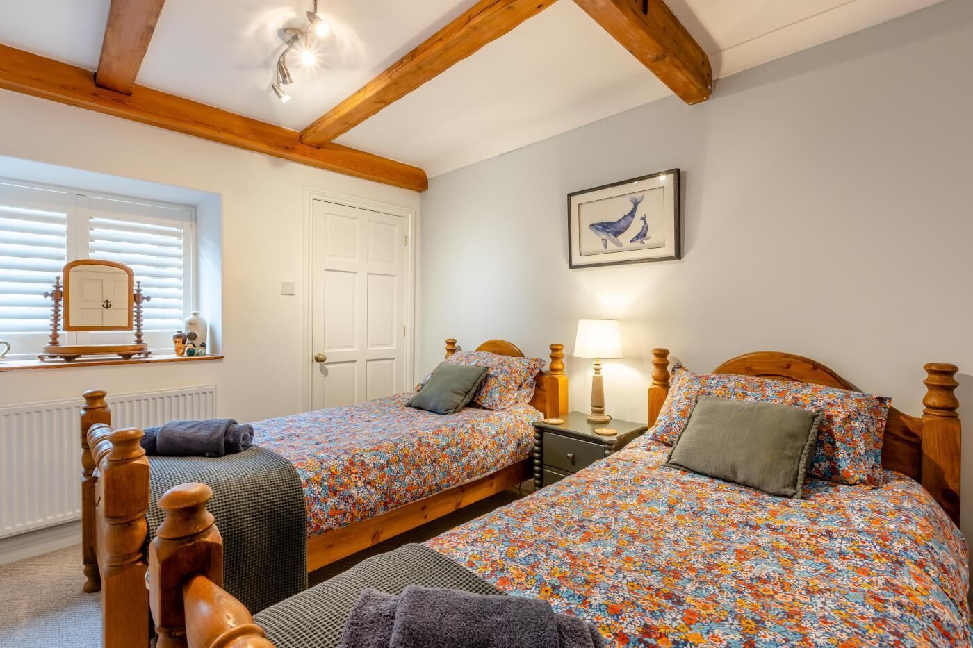 Une chambre à coucher avec deux lits en bois, une fenêtre avec des stores, une porte et un tableau encadré au mur.