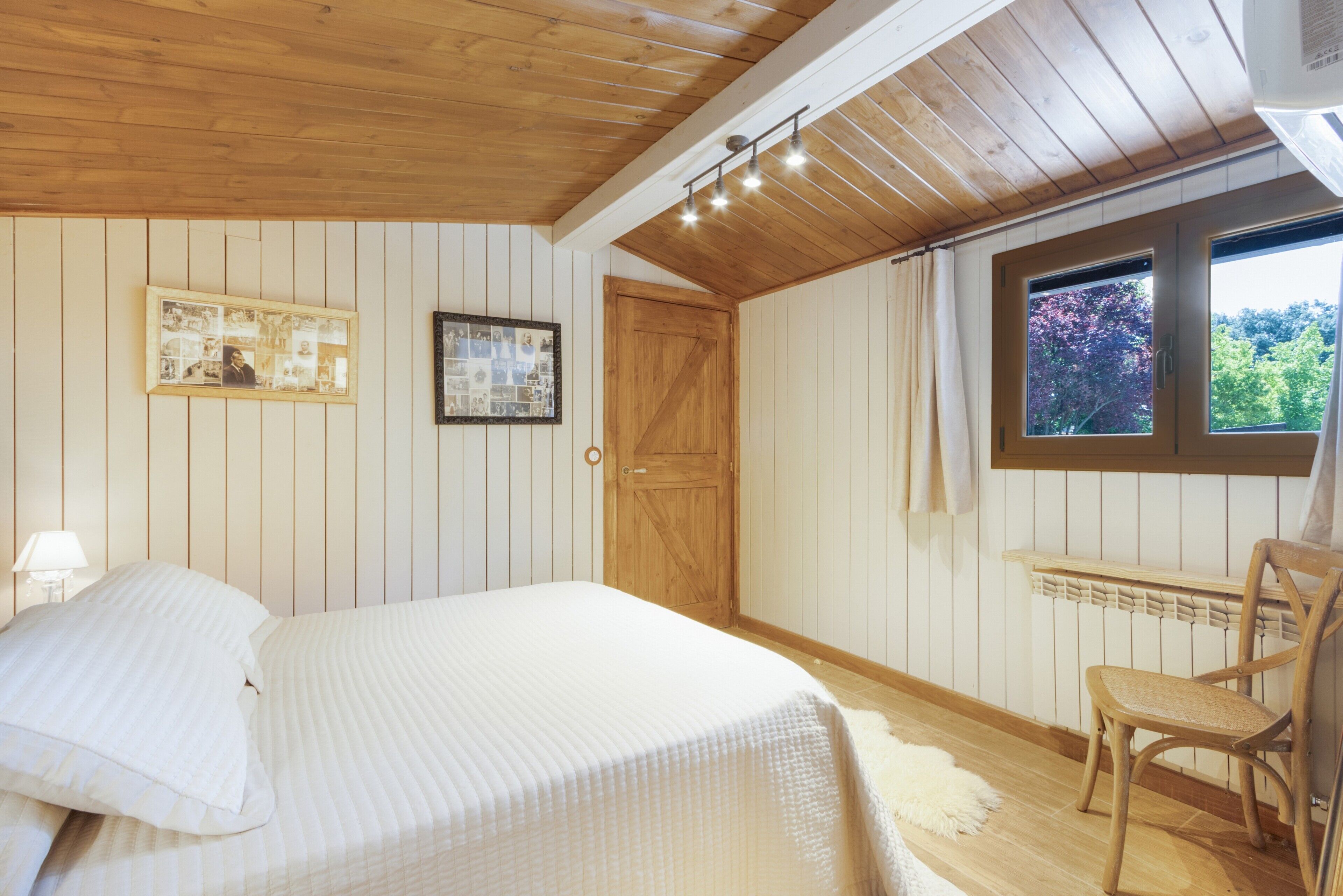 A bedroom with a bed, a chair, a wooden door, and a window with a view.