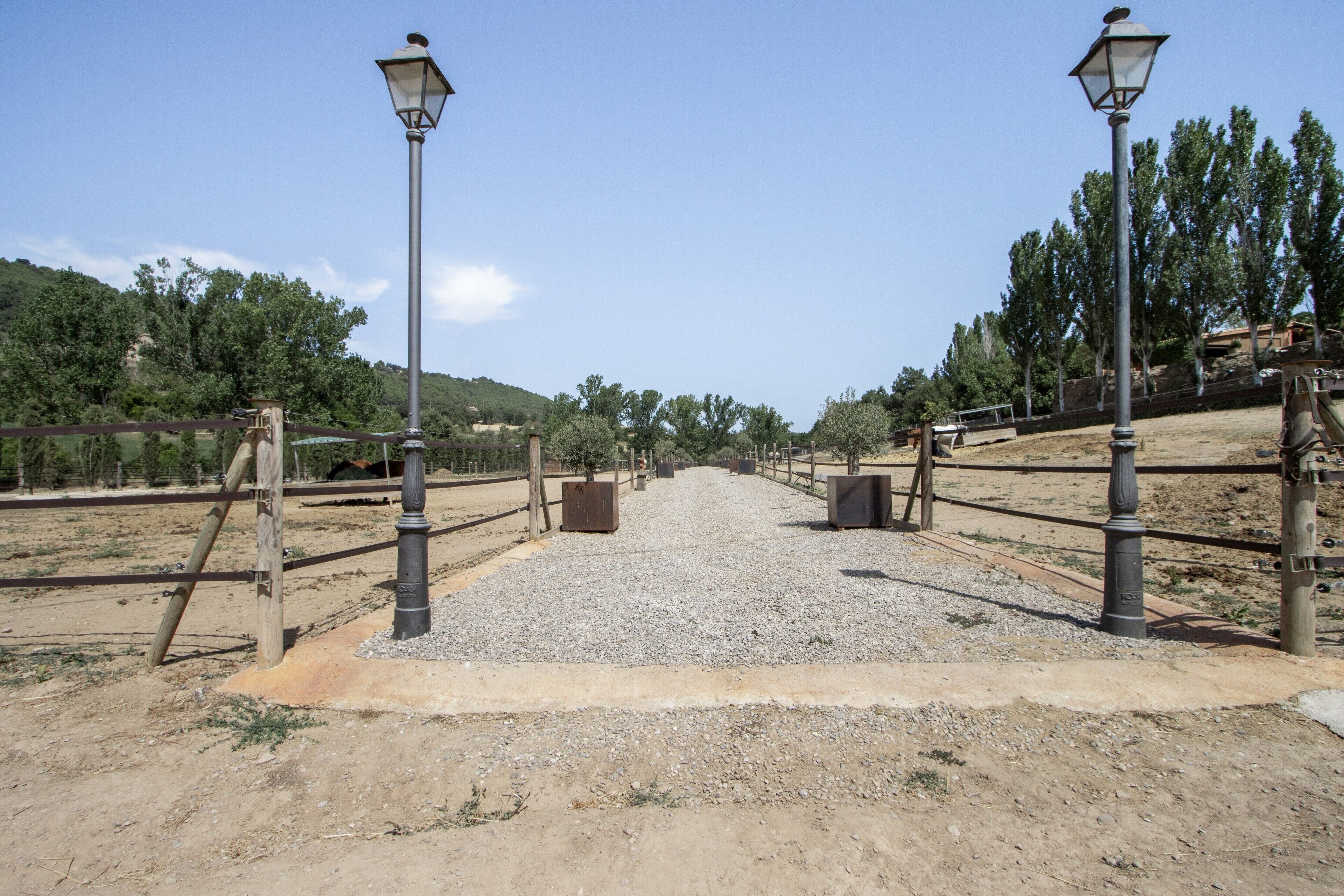 A gravel pathway leading to a fenced area with lamp posts and a gate.