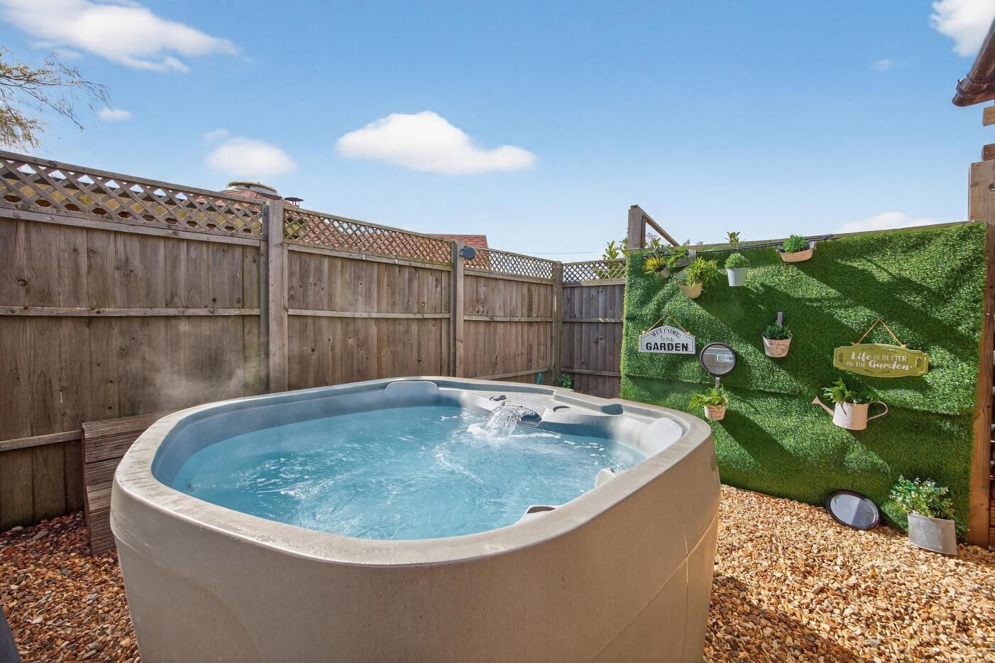 A hot tub in a backyard with a wooden fence, a green wall with potted plants, and a sign that says 'Life is better in the garden.'