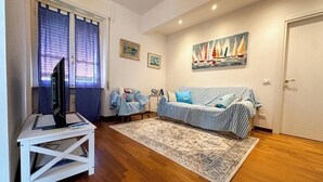 Un salon avec un canapé, un téléviseur posé sur un meuble, un tapis à motifs et un tableau représentant des voiliers.