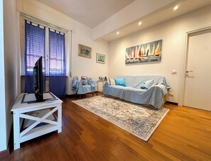 A living room with a sofa, a television on a stand, a patterned rug, and a painting of sailboats. - Top floor with a spacious terrace, parking space, air conditioning, and an elevator (Lerici)