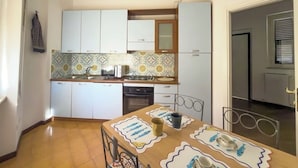 Une cuisine compacte avec des meubles blancs, un pare-feu en carrelage et un coin repas avec une table dressée pour deux personnes.