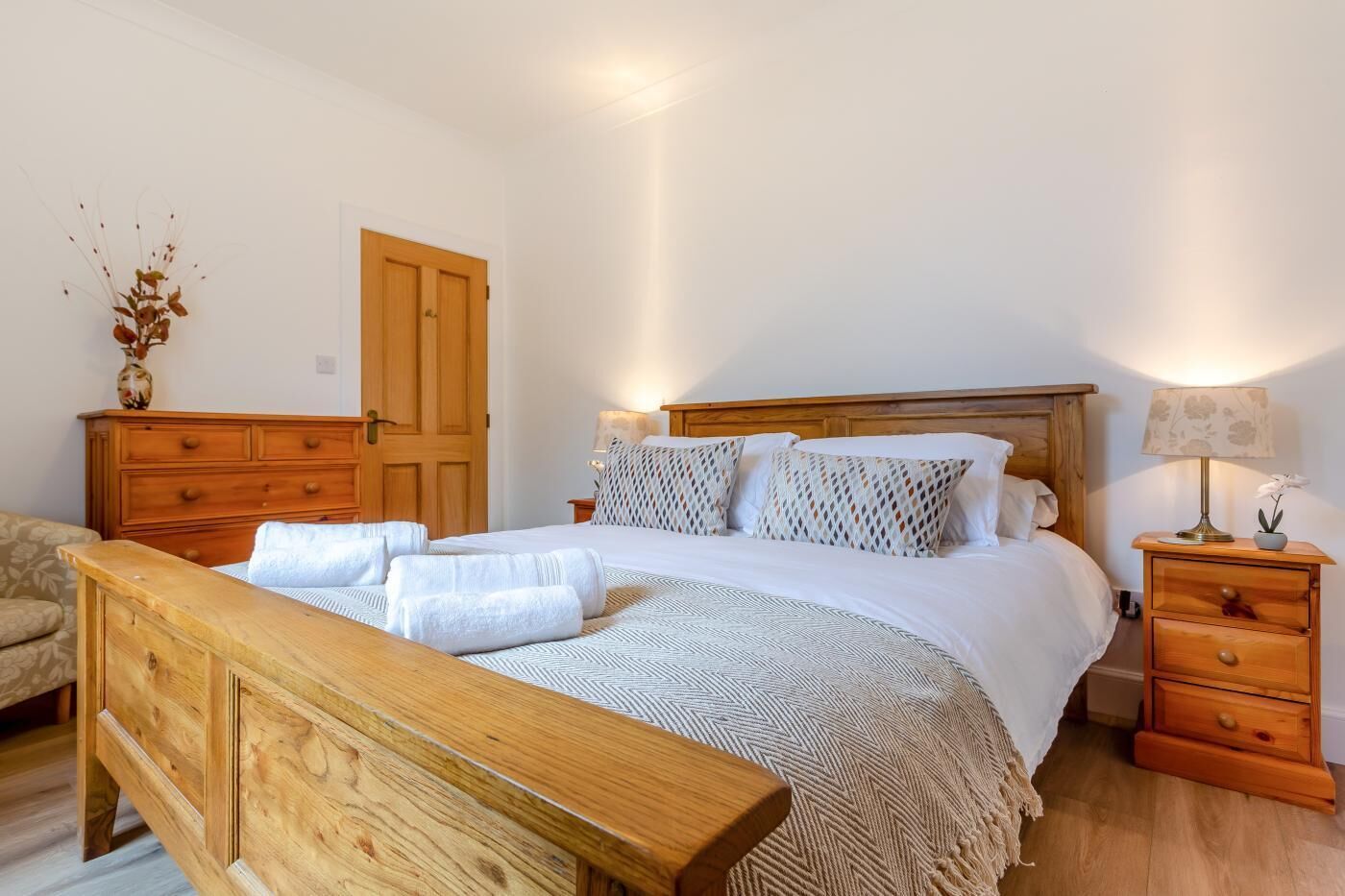 Un dormitorio con cama de madera, mesita de noche con lámpara, cómoda y una puerta.