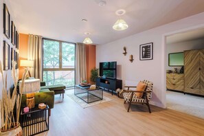 A modern living room with a sofa, armchair, TV, and decorative items. - 2BR Apartment in Manchester - Free Parking (Stretford)