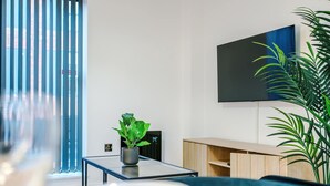 Ein modernes Wohnzimmer mit einem Glastisch, einer Couch, einem an der Wand befestigten Fernseher und einer Topfpflanze.