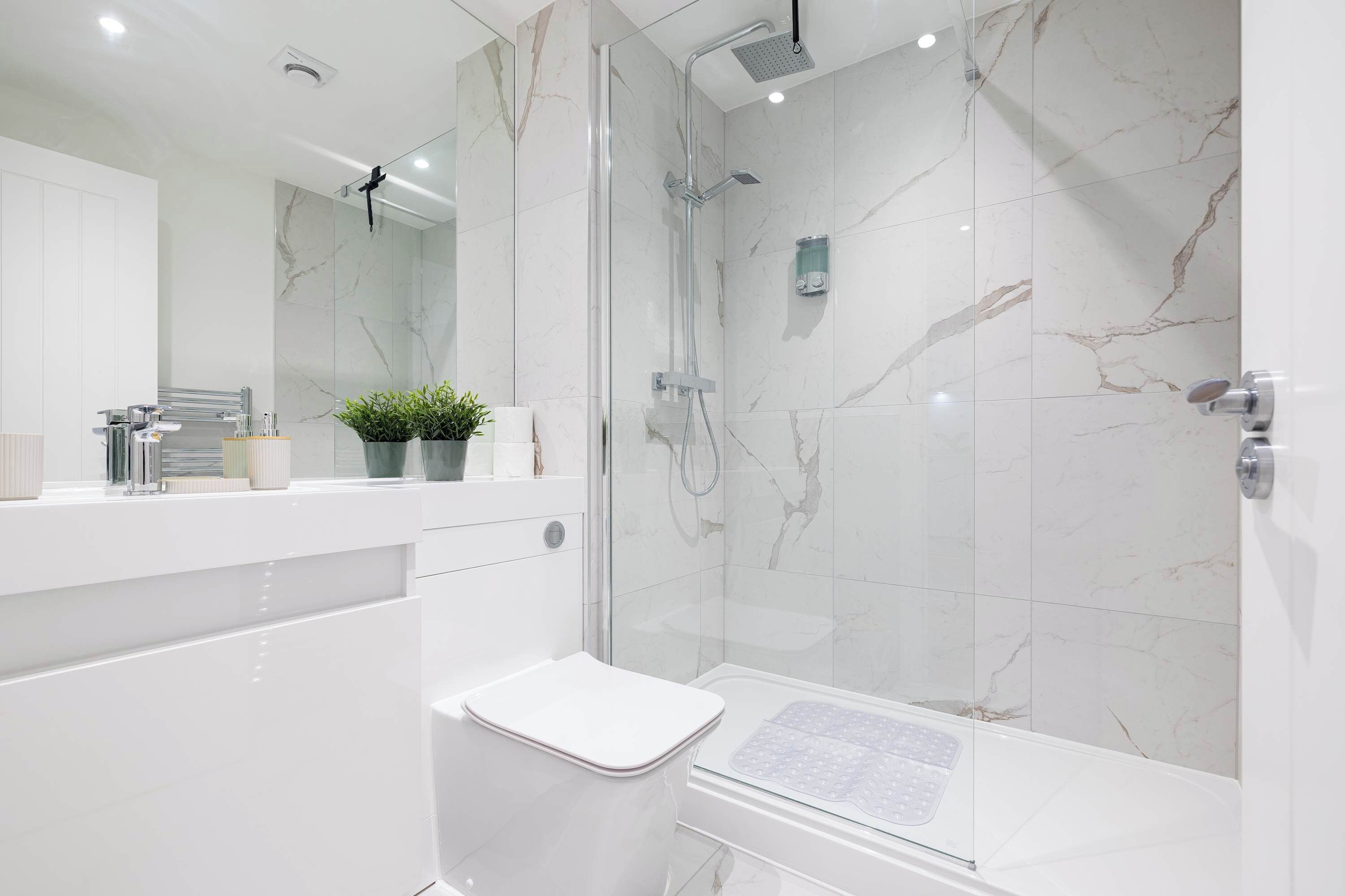 A modern bathroom with a glass-enclosed shower, a white sink, and a marble-tiled wall.