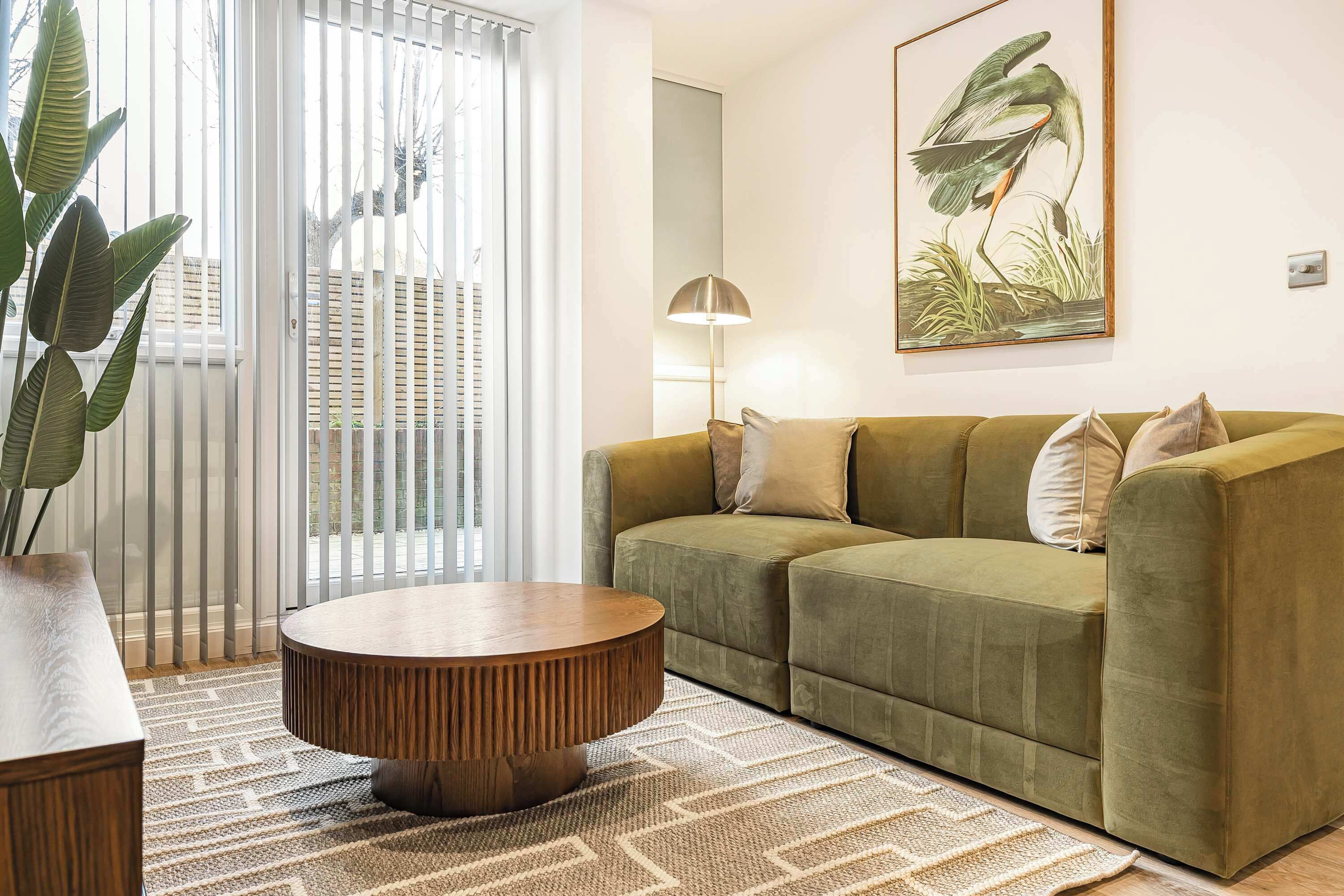 A living room with a green sofa, a round coffee table, a large plant, and a painting on the wall.