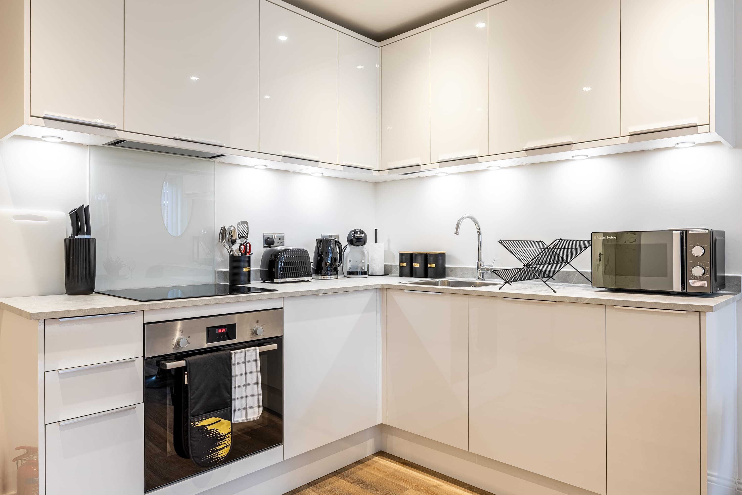 Een moderne keuken met witte kasten, een ingebouwde oven, een magnetron en een spoelbak.