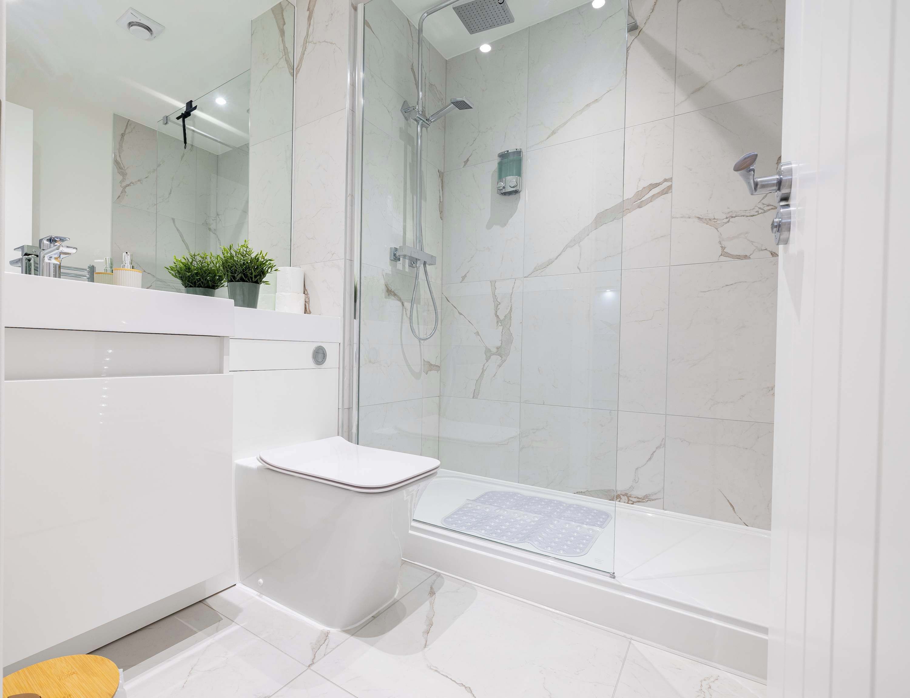 Une salle de bain moderne avec une douche à parois de verre, des toilettes blanches et un sol carrelé en marbre.