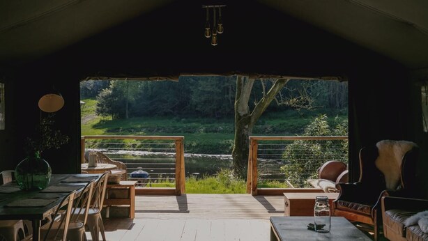 Ein gemütliches Interieur mit einem Holztisch und -stühlen, einer Couch und Blick auf Fluss und Wald.
