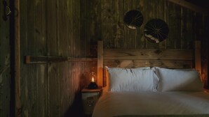 Ein rustikaler Holzraum mit einem Bett, einem Nachttisch mit Lampe und zwei an der Wand befestigten, runden Objekten.