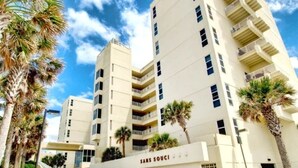 Et hotel med flere etager, en hvid facade, balkoner og palmer.