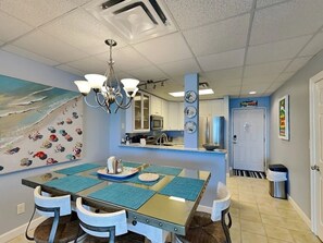 A dining area with a glass table, blue placemats, and a chandelier. - Beautiful 3 BR condo beach front view at San Souci just steps away from paradise (Pensacola Beach)