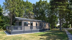 Ein Bungalow mit umzäunter Terrasse, umgeben von Bäumen und einer Rasenfläche.