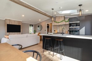 A modern kitchen with a central island, bar stools, a flat-screen TV, and a dining area with a wooden table and chairs. - 2 Bed in Pocklington (oc-o39068) (Pocklington)