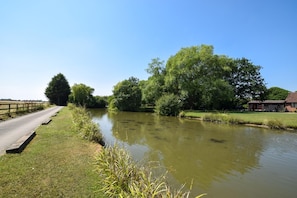 Ein ruhiger Fluss mit Holzzaun und einem Gebäude auf der rechten Seite.