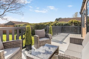 A patio with wicker furniture, a glass table, and a view of a garden and neighboring houses. - 2 Bed in Pocklington (oc-o39068) (Pocklington)